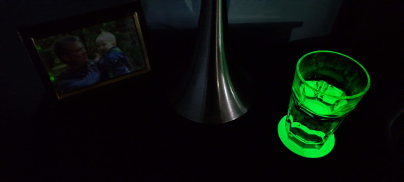 A dark bedside table with a water glass on a 3.5" Slumberlights glow coaster and a family picture.